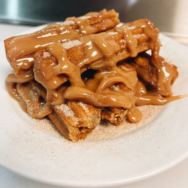 Brazilian churros drizzled with dulce de leche and sprinkled with sugar on a white plate.