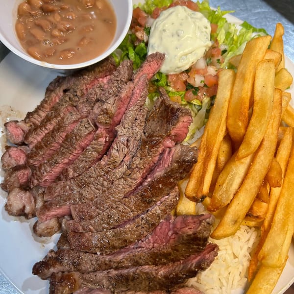 Brazilian steak plate with sliced beef, rice, fries, salad, and a side of beans.
