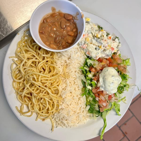 A Brazilian plate with spaghetti, rice, beans, potato salad, and a green salad with pico de gallo.