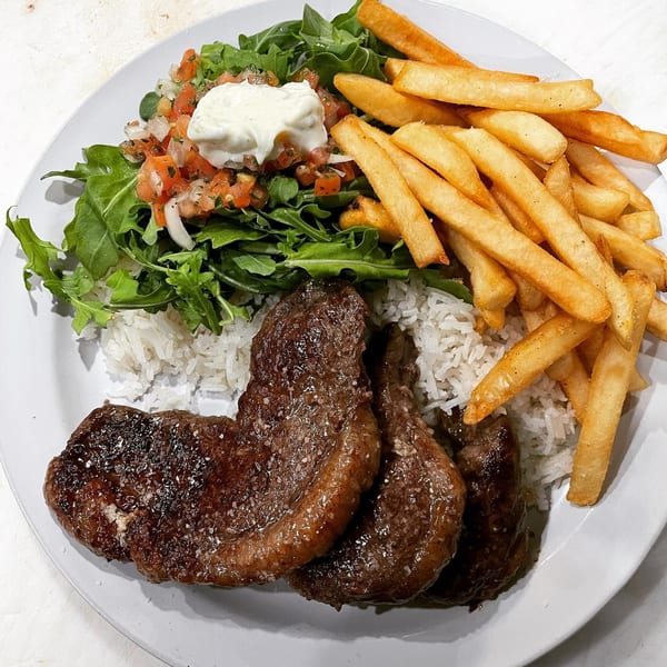 Brazilian picanha steak with rice, fries, and a fresh salad topped with pico de gallo and cream.