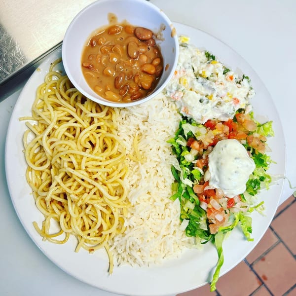 A Brazilian plate with spaghetti, rice, beans, potato salad, and a fresh green salad with dressing.