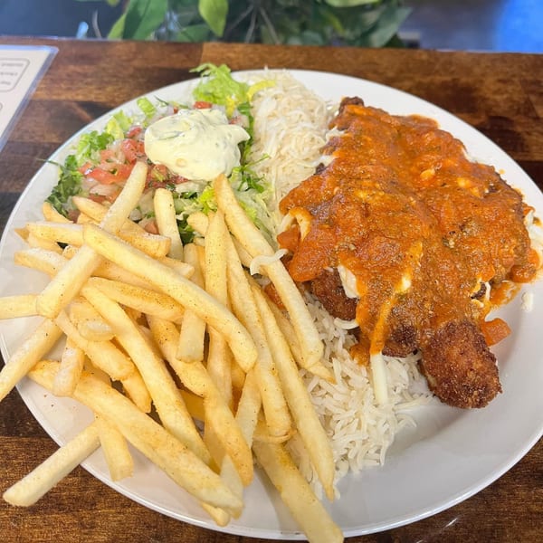 A Brazilian dish with fried chicken covered in red sauce, rice, salad, and french fries.