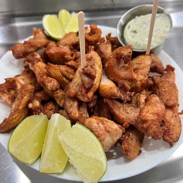 Aroma do Brazil's fried chicken pieces with lime wedges and a dipping sauce.