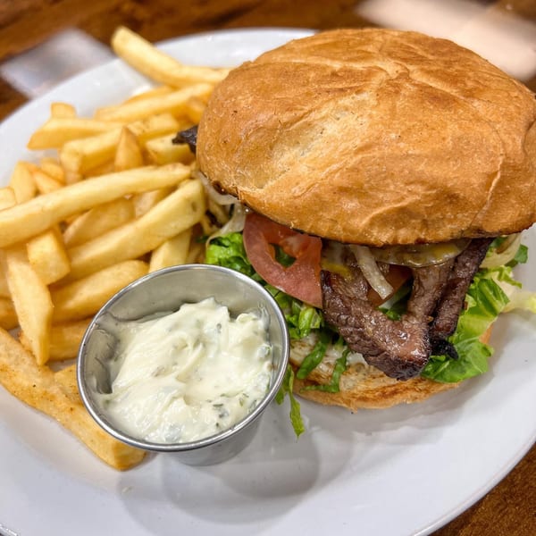 A Brazilian steak sandwich with lettuce, tomato, and onions, served with fries and a side of sauce.