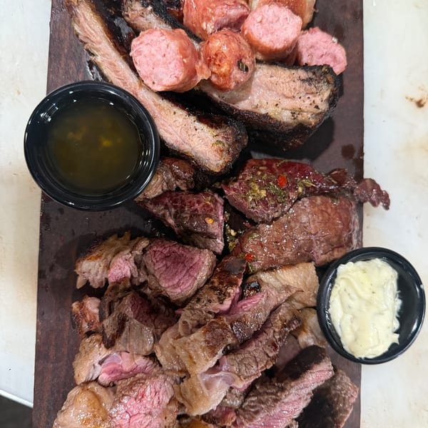 Aroma do Brazil's platter of grilled meats, including sausages, steak, and ribs, with two dipping sauces.