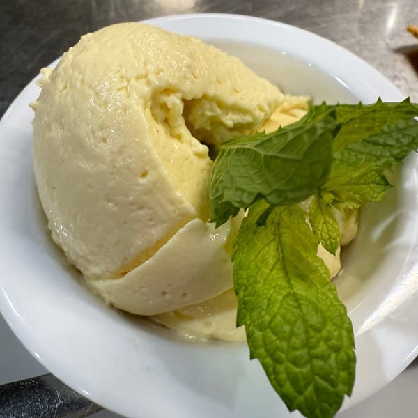 A white bowl filled with creamy, light yellow Brazilian dessert, garnished with fresh mint leaves.