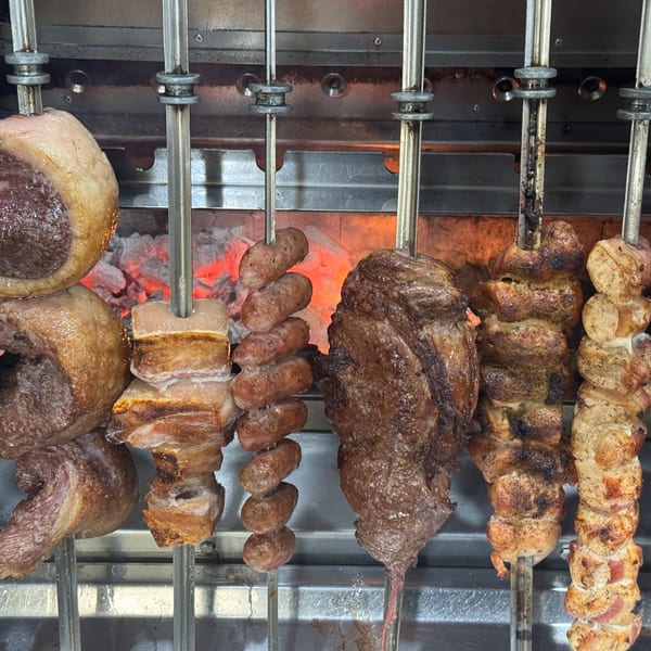 Various Brazilian meats, including picanha, sausages, and pork belly, cooking on skewers over hot coals.